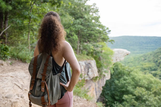 A caucasian woman in her 30s stands along the edge of a cliff looking at Whitaker Poin